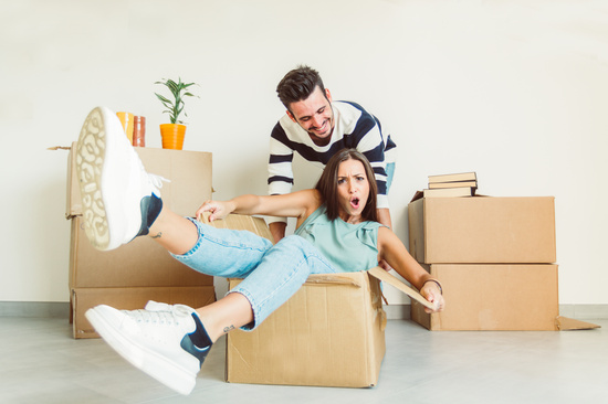 Happy couple having fun moving in the new house playing riding cardboards